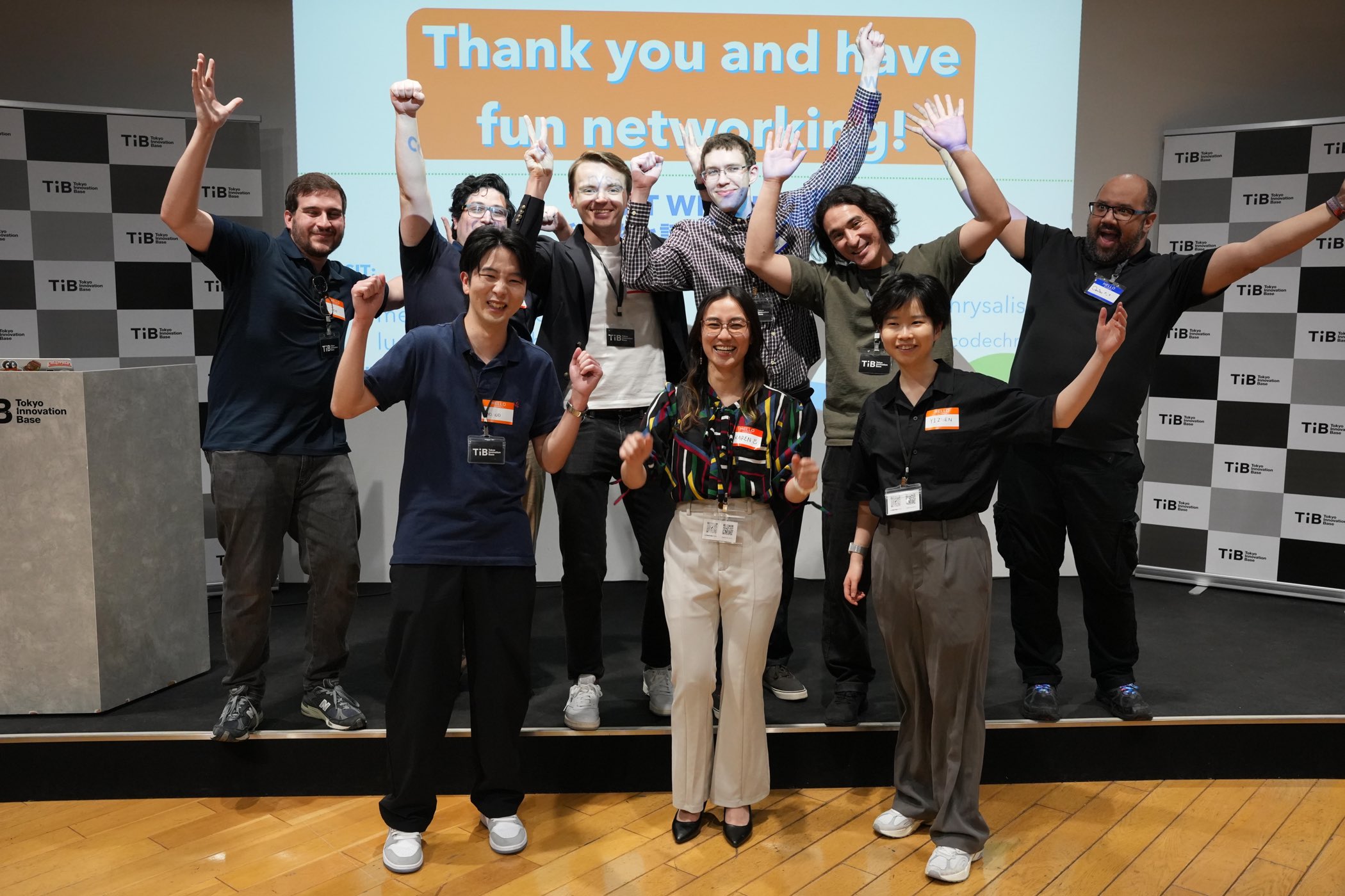 The Code Chrysalis cohort on stage at Tokyo Innovation Base with arms raised, in front of a slide reading Thank you and have fun networking