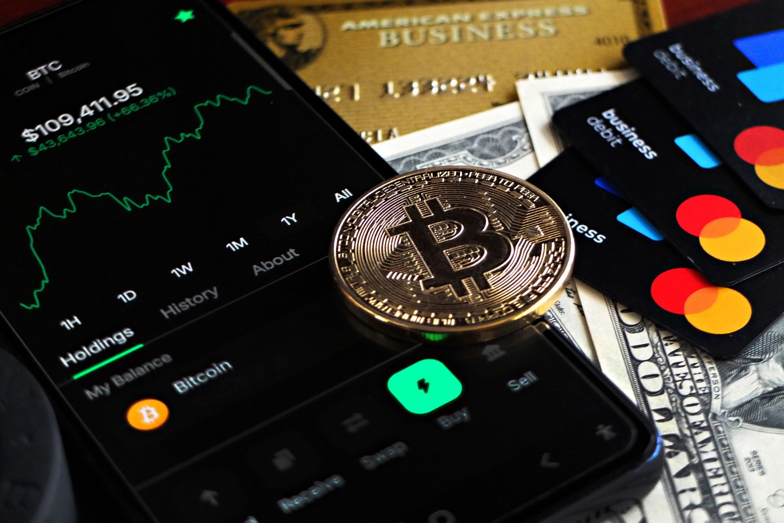 A crypto coin resting on payment cards next to a phone showing a price chart