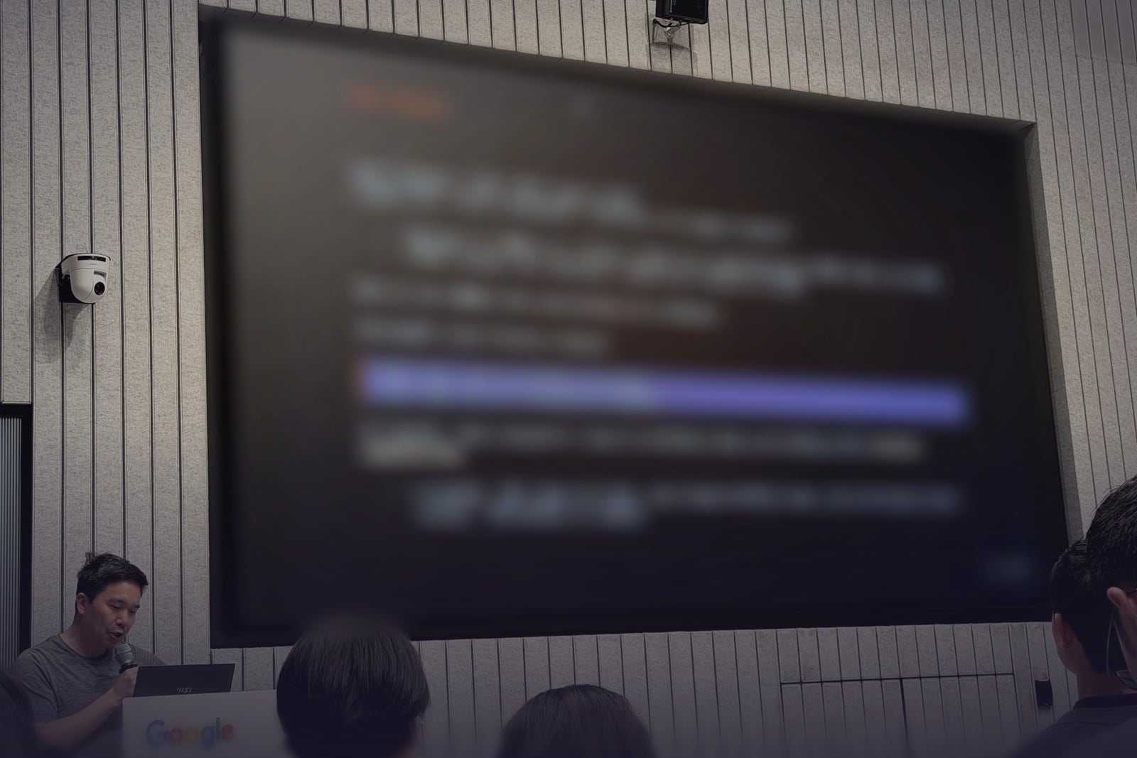 A speaker at a Tokyo AI meetup presenting a slide titled Dark Factory to a seated audience, the slide deliberately blurred