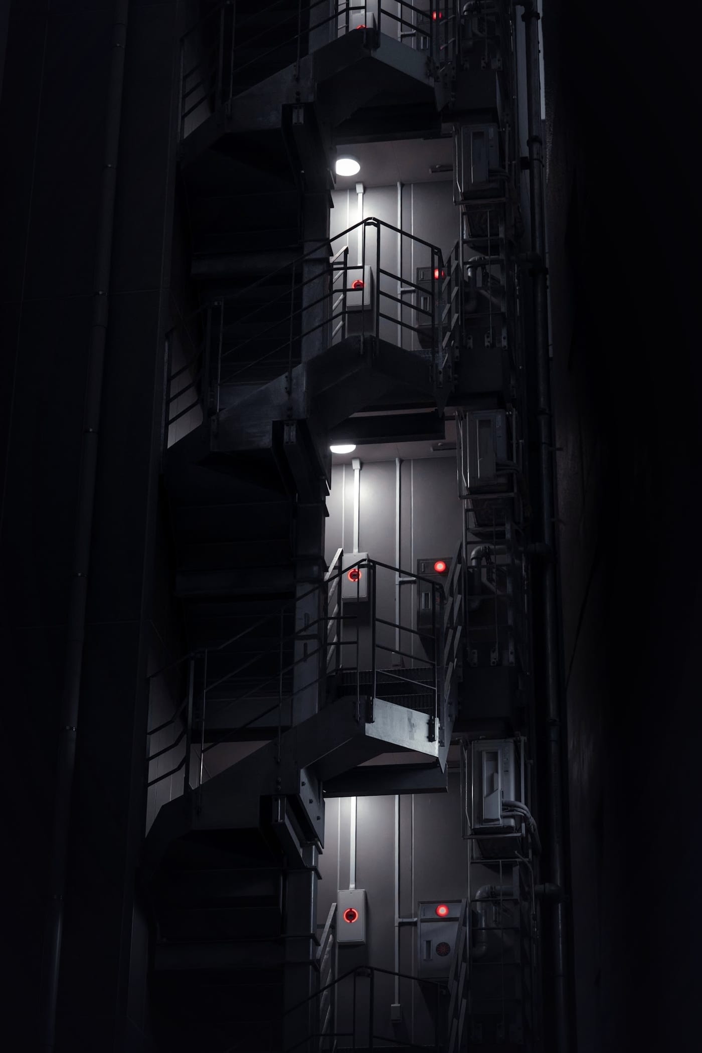 A dark industrial stairwell lit only by a few emergency lamps and red indicator lights, with nobody on the stairs